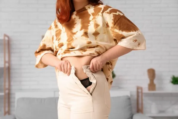 Image of woman trying to do her trousers up after pregnancy weight gain Edgware